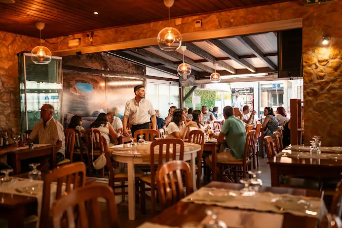 Sala do Restaurante & Pizzaria Catarina cheia ao almoço, com paredes de pedra e mesas de madeira